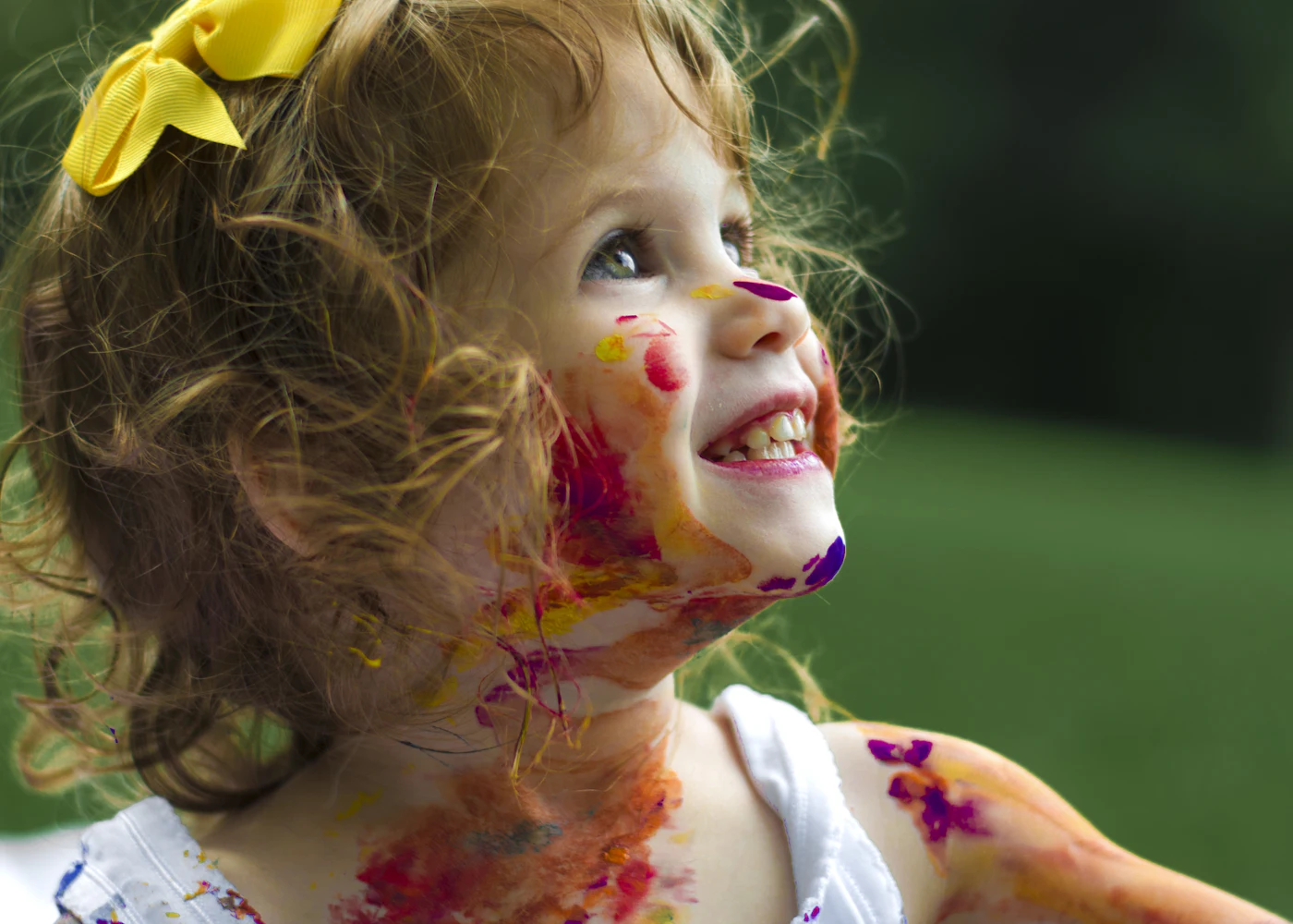 A little girl laughing mid-craft with paint on her face and hands