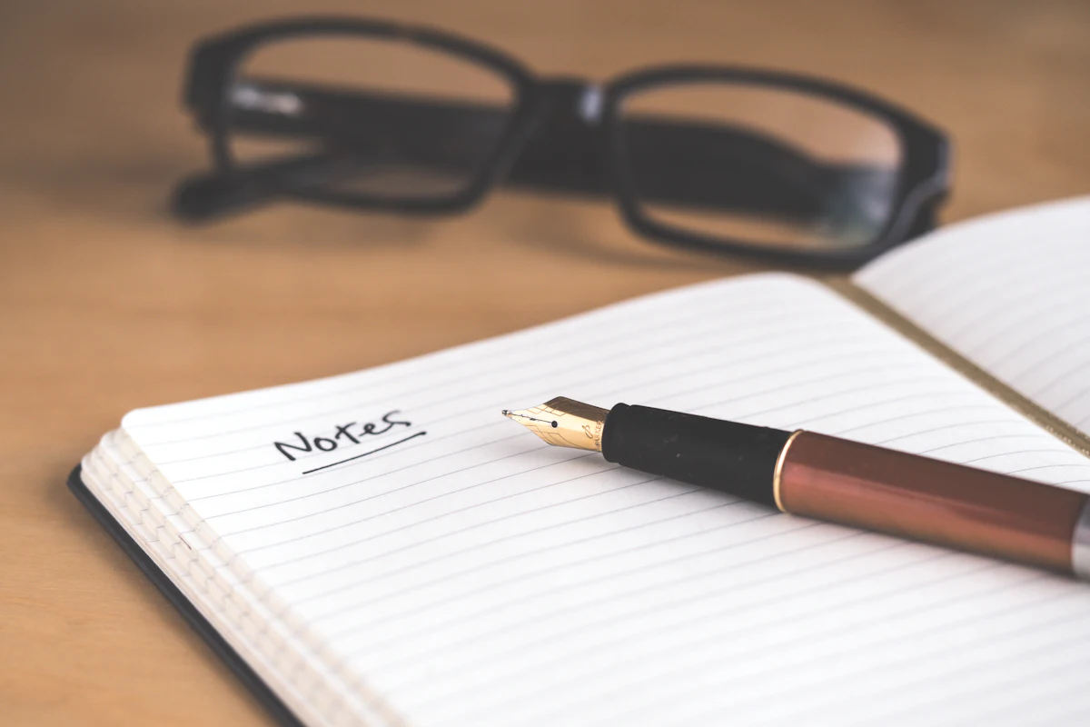 A notebook labeled notes with a pen and reading glasses